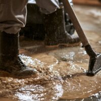 Worker cleaning muddy water with a floor extractor in boots.