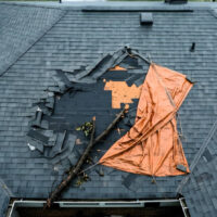 Damaged roof with a tarp and fallen tree branch.