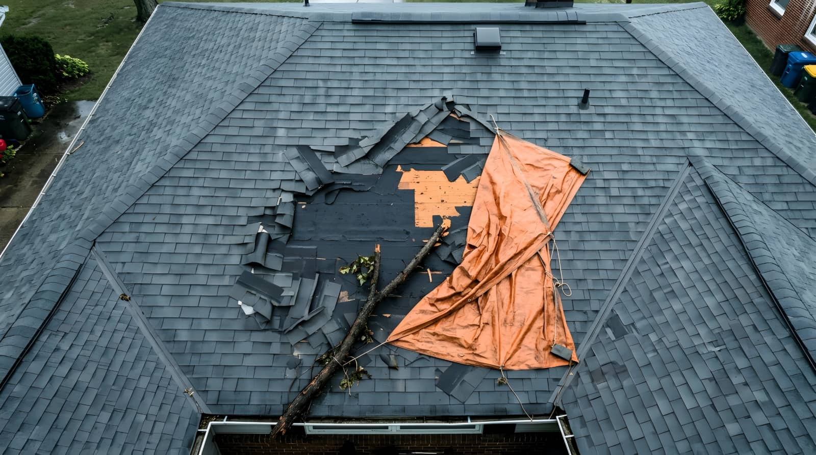 Damaged roof with a tarp and fallen tree branch.