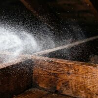 Water spraying from a leak onto wooden beams in a dark attic or crawl space.