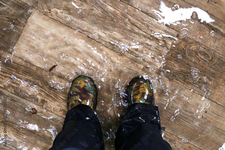 Booted feet standing on a wood floor, with water coming up to the ankles.