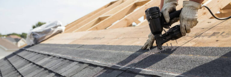 Worker nailing roofing felt on a house roof.