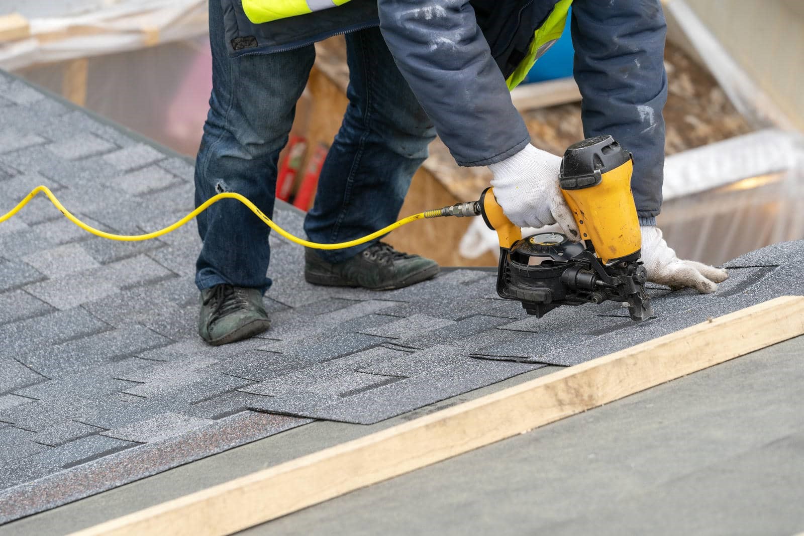 Worker using a nail gun to install asphalt shingles on a roof.