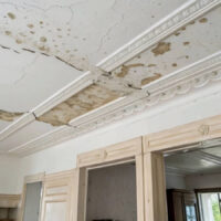 Water-damaged ceiling with cracks and peeling plaster in a room.