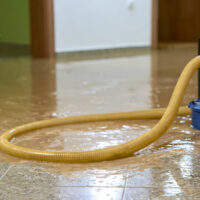 Flooded hallway with a water pump and hose draining water.