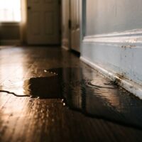Water leaking onto a hardwood floor in a hallway.