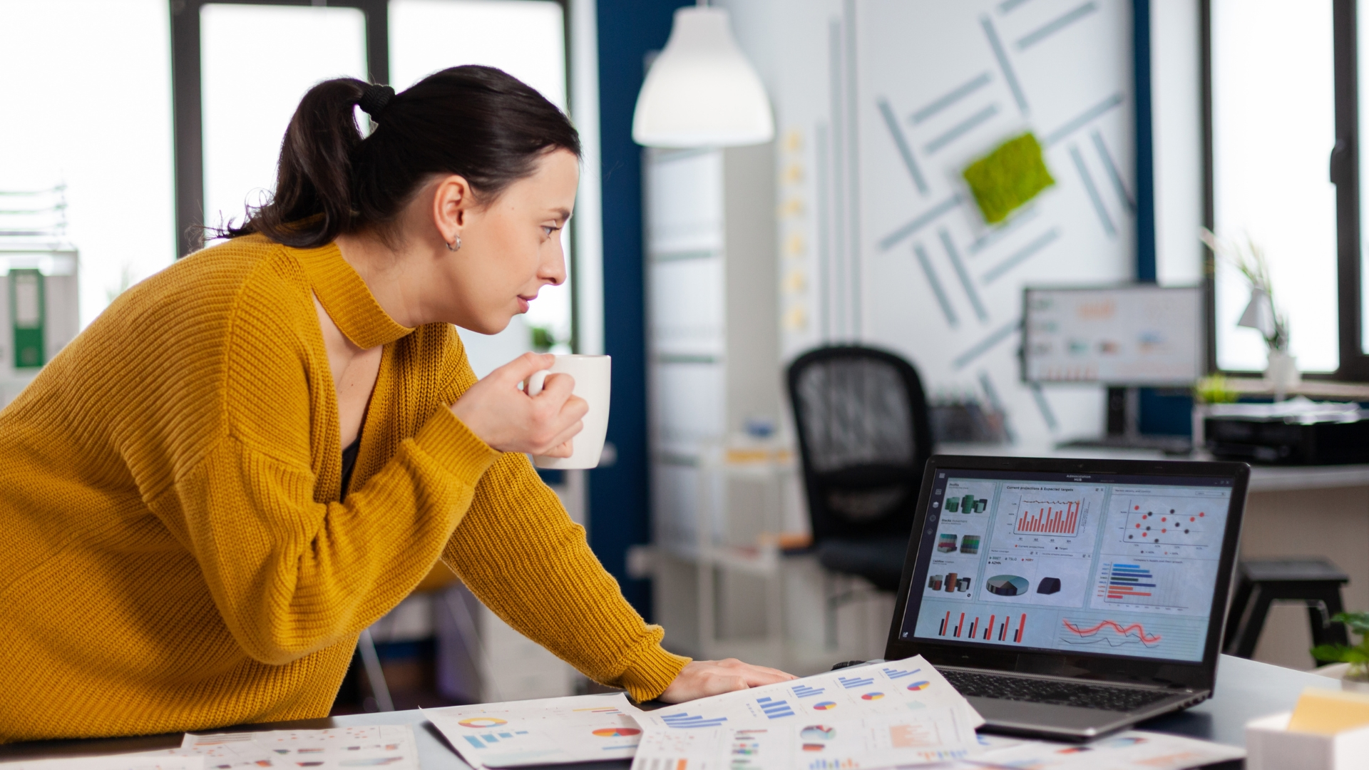 An accomplished Caucasian businesswoman in a modern corporate office, confidently analyzing online statistics on her laptop. Enjoying a cup of coffee, she exudes professionalism and success as an executive entrepreneur. With a backdrop of documents and a profitable graph, she showcases her leadership and expertise. Her workplace reflects a bustling and technology-driven environment, symbolizing her role as a successful manager. This portrait captures a dedicated businesswoman, embodying the modern career woman, while also promoting the best water damage company.