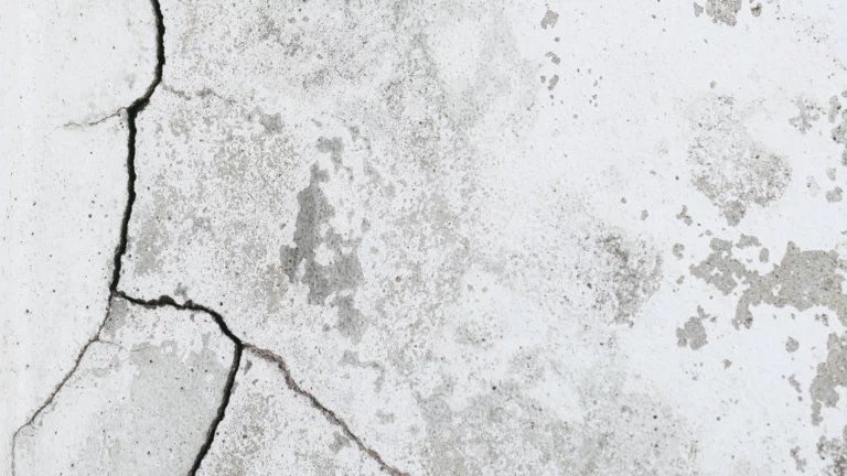 A close-up photograph of a water wall in a wet house. The concrete cement surface is visibly damaged and cracked, with water leaking and forming puddles. The water leakage is evident as a white discoloration on the surface. This image illustrates the need for immediate attention and repair to prevent further water damage. Learn how to repair water damage to prevent such leaks and maintain the integrity of your property.
