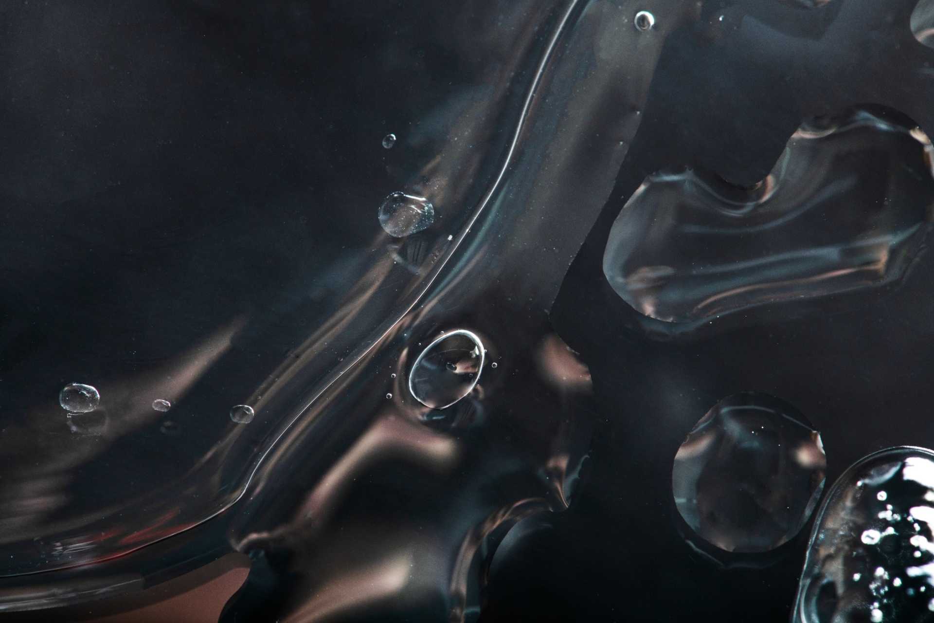 A close-up view of a black water background adorned with mesmerizing bubbles. The abstract nature of this image captivates with its fluid motion and textured surface. The high-definition photography showcases the intricate details of the droplets and the captivating shapes they create. This unique underwater composition offers a blank space for design purposes and provides a visually striking wallpaper option. The dark background enhances the captivating effect of the liquid, making it an ideal choice for artistic and aesthetic applications.