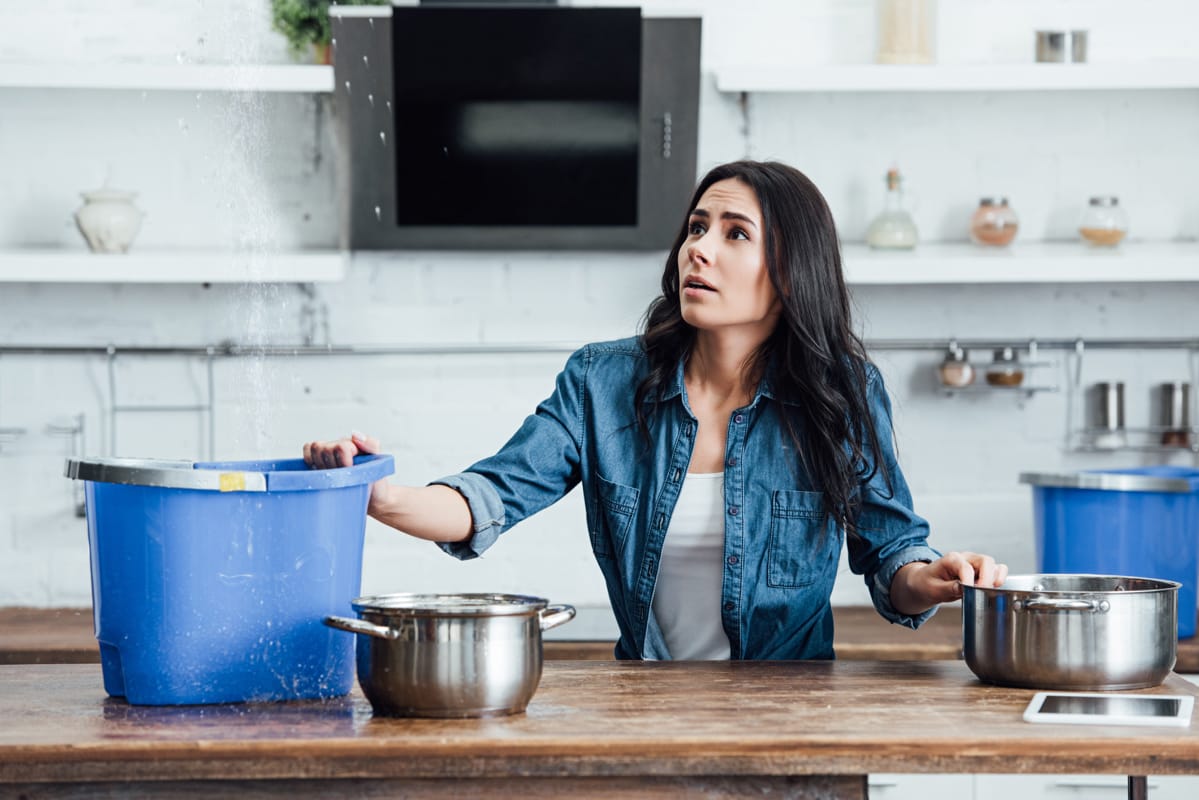 A woman wonders HOW LONG DOES WATER DAMAGE RESTORATION TAKE, while holding buckets for water seeping through her ceiling.